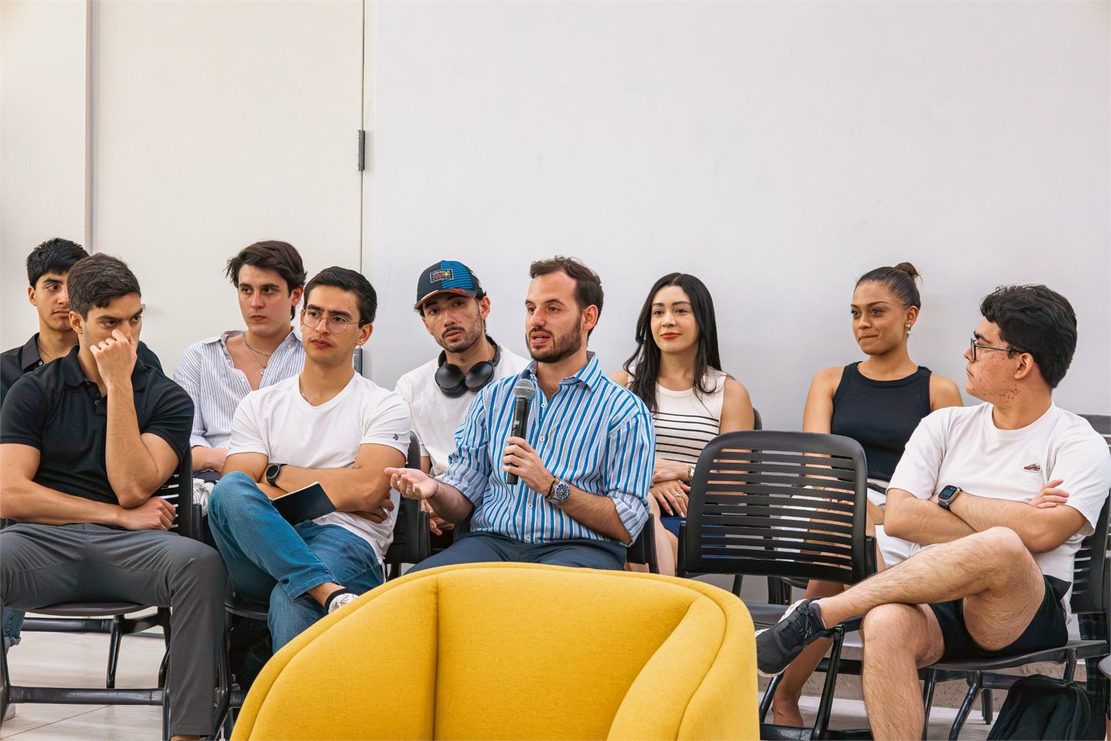 A room of people listening while one of them speaks into a microphone.